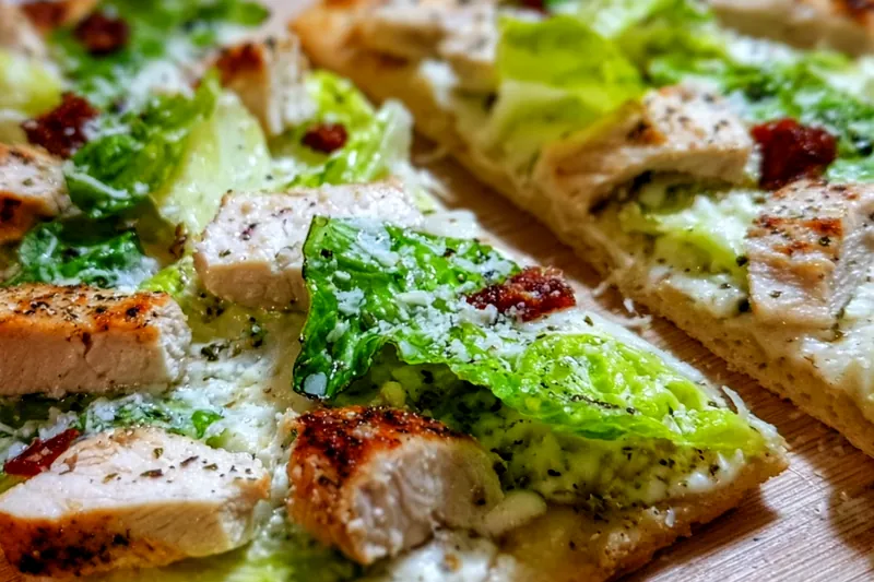 Fresh ingredients for chicken caesar flatbread including flatbread, raw chicken breast, romaine lettuce, Caesar dressing, and Parmesan cheese arranged on a marble counter